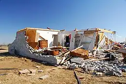 The remains of a home, now mostly a pile of rubble; part of the structure remains intact.