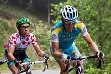 Thomas Voeckler wearing a white jersey with red polka dots, following Fredrik Kessiakoff as they ride up an incline