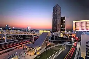 A train station built over a busy intersection in front of several skyscrapers at sunset.