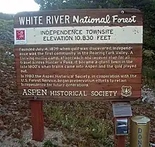 A brown wooden plaque with "White River National Forest" inscribed across the top and explanatory text about the Independence Townsite below