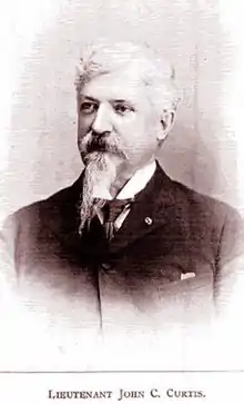 Head and shoulders of an older white man with Van Dyke mustache and goatee wearing a dark suit over a white shirt and dark tie. Below are the words "LIEUTENANT JOHN C. CURTIS".