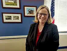 Photograph of Undersecretary Moffitt in her office in front of American flag with pictures of her family's organic walnut farm in background