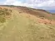 A hillside covered in bracken and scrub with a grassy path going up the hill, first to the left then to the right