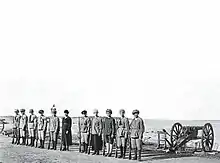 Eleven armed women at attention next to a cannon