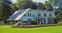 A long white house with some stone at the back and a pointed, sloping roof at the front