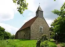 A small simple stone church with a red tiled roof and a wooden bellcote