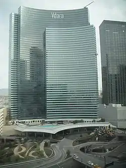 Elevated view of a construction site; at center is the partially completed steel frame of a curved building. Several cranes and construction vehicles are visible.