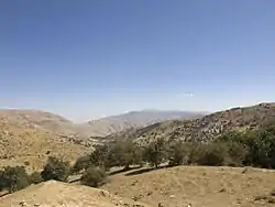 Photo of arid hills with sparse vegetation and trees in the foreground