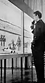 Man stands in front of a display case with rimonim, torah crowns and torah wimpels.