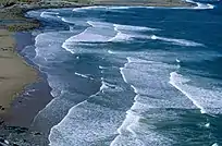 Foam edged waves create a scalloped pattern on a sloping sandy beach