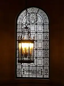 A round-arched window with a complicated iron and glass decoration. A lantern-like light fixture hangs in front. At the bottom of the window is written "Go forward without fear and with manly heart", a quotation attributed to Abraham Lincoln. The words "AD 1919" are also visible in the top of the glass in stylized script.