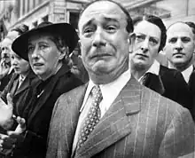 A Freshman in front of a well dressed crowd crying while appearing to be suppressing his emotions by pressing his lips and contorting his forehead