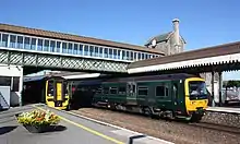 Two green trains beneath a lattice bridge