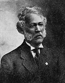 Black and white portrait of a man, wearing suit, with a white collared shirt and a black necktie, with a star on his jacket's lapel.