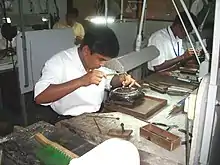 A Sri Lankan man works on some jewellery on a worktop lit by overhead lamps.