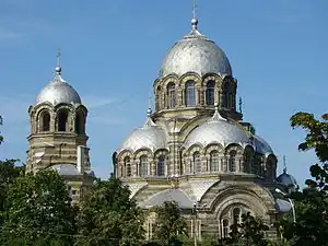 The church of the Theotokos Orans (Our Lady of the Sign) in Vilnius  demonstrates typical features of developed Byzantine revival: exposed two-tone, striped, masonry; four symmetrical apses tightly fused into the main dome, creating a tall triangular outline; arcades blending into the domes; and a relatively small belltower, clearly subordinate to the main dome.